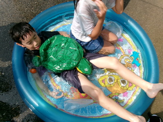 新聞紙とガムテープで作ったカメを抱っこしてプールに入っている男の子